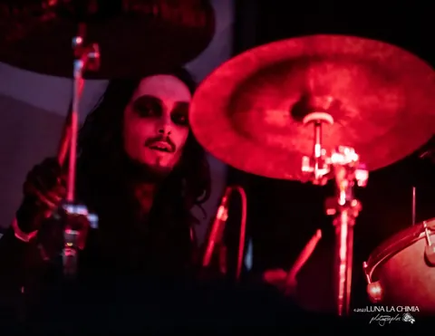Drummer in white face paint behind a red cymbal