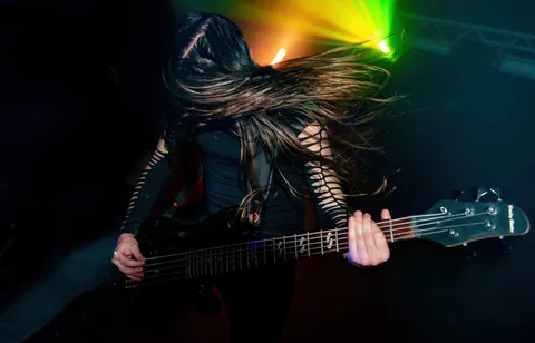 Bassist mid headbang, hair flying under green light