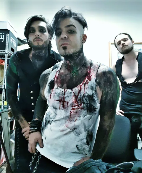 Three band members backstage, one shirt stained with fake blood