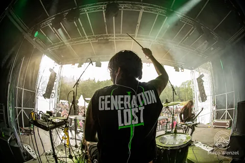 Drummer seen from behind in a Generation Lost shirt, facing the festival crowd