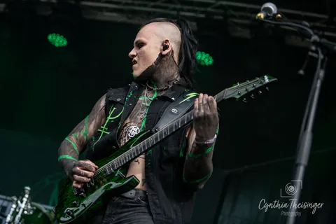 Guitarist with a green guitar and green light on his tattoos