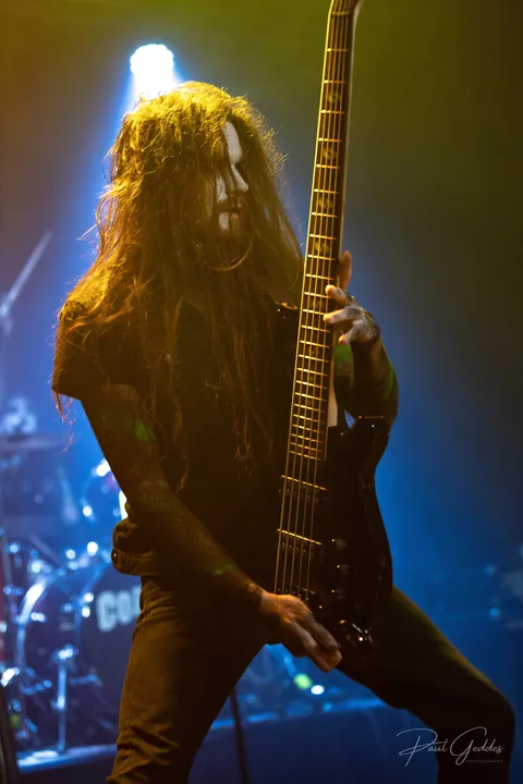 Bassist with long hair lit from behind in gold and blue